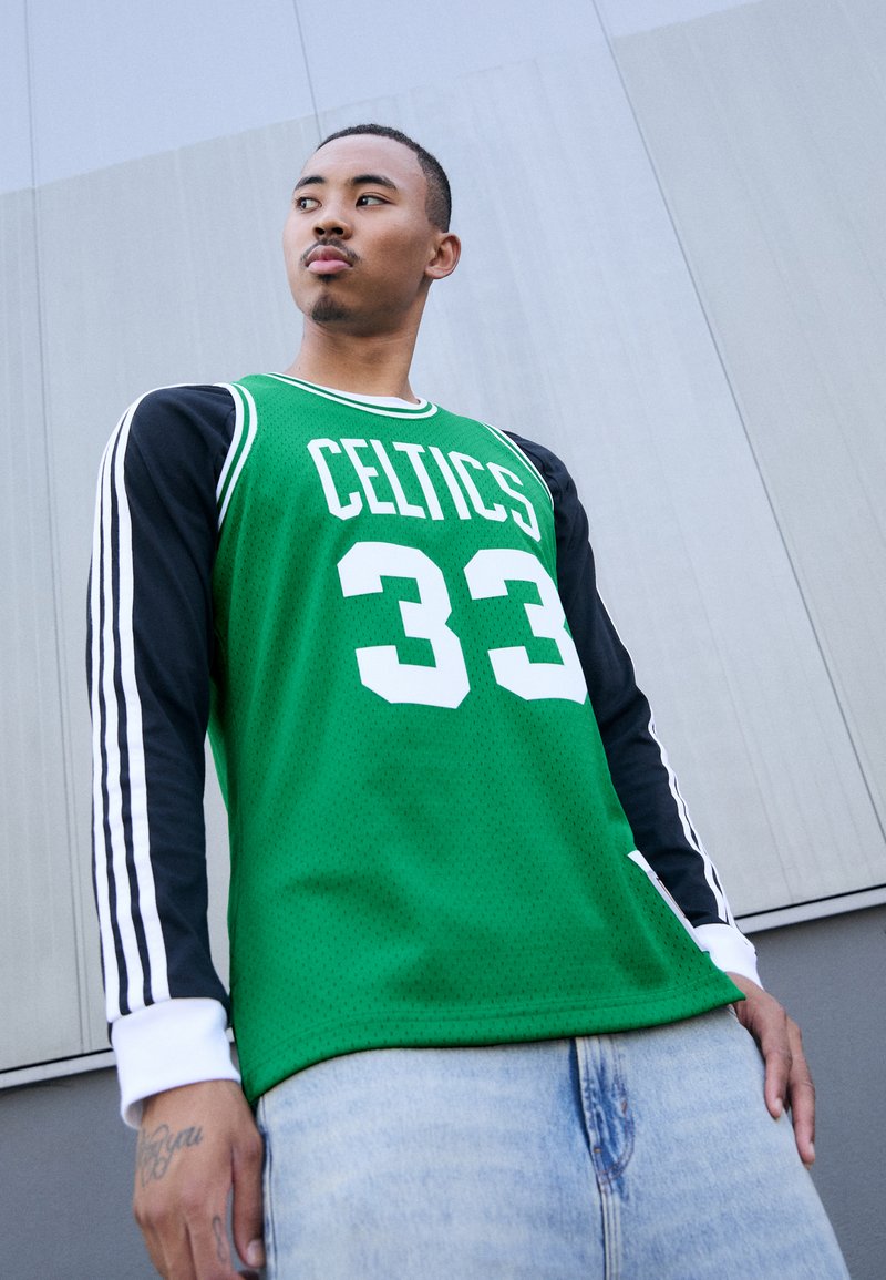 Grünes Basketballtrikot mit weißem "Celtics"-Text und der Nummer 33, ausgestattet mit schwarzen langen Ärmeln mit weißen Streifen und einer strukturierten Oberfläche.