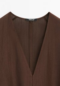 Robe en lin marron à décolleté en V profond avec des lignes de couture visibles et une étiquette noire indiquant "Massimo Dutti Made in Portugal" à l'intérieur du col.