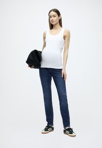 Λευκό αμάνικο τοπ, σκουρό μπλε τζιν και μαύρα αθλητικά παπούτσια με λευκές λεπτομέρειες. Το μοντέλο κρατάει μια μαύρη τσάντα. Απλός, εφαρμοστός σχεδιασμός.