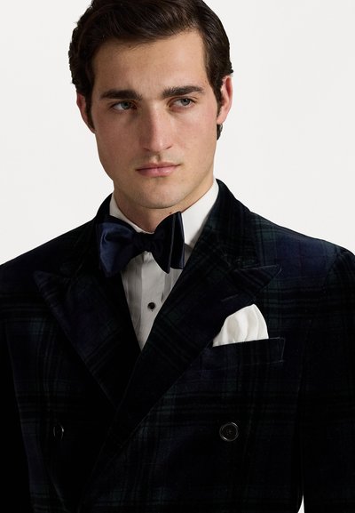 Veste de smoking en velours à carreaux sombres avec un design à double boutonnage, comprenant des boutons noirs, un mouchoir de poche blanc et un nœud papillon bleu marine.