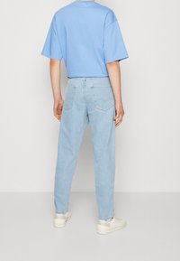Camiseta recortada de color azul claro con mangas cortas; combinada con unos vaqueros de corte holgado en un lavado claro que cuentan con dos bolsillos traseros y un sutil detalle de costura.