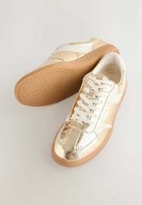 Goldfarbene Metallic-Sneaker mit weißen Akzenten, featuring einem glatten Design, einer strukturierten Gummisohle und weißen Schnürsenkeln. Perforierte Details an der Spitze.