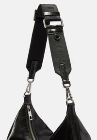 Czarny skórzany pasek torebki z teksturowanym fragmentem tkaniny, metalowymi elementami oraz widocznym detalem zamka błyskawicznego z jednej strony.