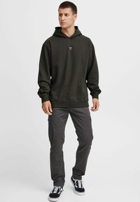Mørkegrøn hoodie med et logo på forsiden, parret med grå cargo-bukser. Sættet har en afslappet pasform, ribbede manchetter og sorte sneakers.