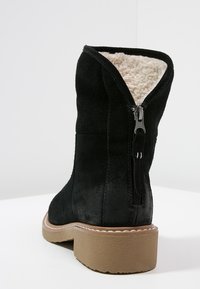 Bottine en daim noir avec une doublure en fausse fourrure, équipée d'une fermeture éclair sur le côté et d'une semelle en caoutchouc texturée. Le talon est bas et épais.