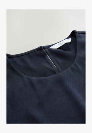 Tumedateine särk ümmarguse kaelusega, tekstuuriga kangast ja taga lukuga. Sildil on kirjas "NEXT". Sile viimistlus ja pehme langevus.