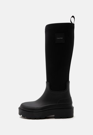 Hoher schwarzer Gummistiefel mit dicker Profilsohle, Zuglasche hinten und kleinem quadratischem Calvin Klein-Logo in der Nähe des oberen Bereichs.