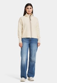 Krämfärgad fleecejacka med hög krage, framfickor och texturerad tyg. Matchad med ljusblå, något lösa jeans.