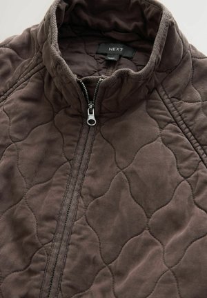 Brown quilted jacket with a high collar and zip closure. Features textured fabric with a diamond pattern and a silver zipper. Brand label visible.