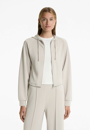 Light beige cropped zip-up hoodie with a soft texture, drawstring hood, and ribbed cuffs, paired with a white top.