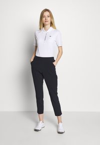 Biała koszulka polo z kołnierzykiem, zestawiona z ciemnogranatowymi spodniami do kostek. Model nosi białe buty sportowe. Prosty design, luźny krój.