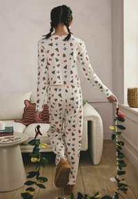 Kinder-Pyjama-Set aus cremefarbenem Stoff mit rot-, grün- und blau-gestreuten, festlichen Mustern. Enganliegender Schnitt mit einem elastischen Bund und bequemen Nähten.