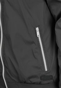 Graue Bomberjacke aus leichtem, glattem Stoff, mit einer weißen Reißverschlusstasche und einem gerippten Bund. Etikett "BLEND" angebracht.