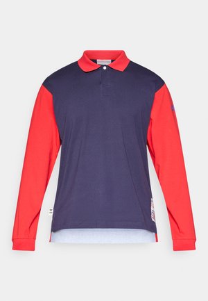 Polo a maniche lunghe con corpo blu navy, maniche rosse e colletto classico. Dettagli notevoli includono un logo e un orlo laterale con spacco.