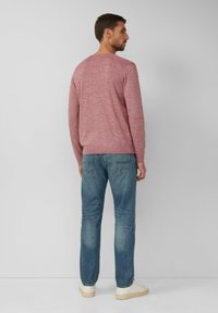 Roter und grauer Melange-Pullover mit Rippbündchen, kombiniert mit hellblauen Straight-Leg-Jeans und weißen Sneakers. Rückansicht.