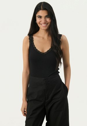 Black tank top with lace trim on the edges, featuring a deep V-neck. Paired with high-waisted black trousers, showcasing a relaxed fit.