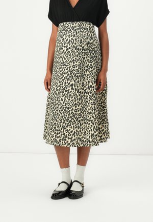 Mujer con una camiseta negra y una falda midi beige con estampado de leopardo negro, combinadas con calcetines blancos y zapatos Mary Jane negros.