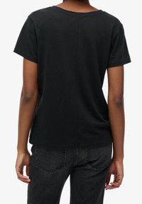 Black cotton t-shirt with a round neckline and short sleeves. Features a subtle seam down the center back, paired with dark jeans.