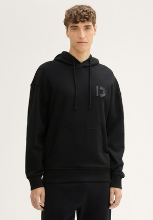 Zwarte hoodie met een gestructureerde afwerking, voorzien van een voorzak en een logo-accent op de borst. Capuchon met trekkoord en een ontspannen pasvorm.
