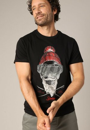 Zwarte t-shirt met korte mouwen, voorzien van een afbeelding van een baardeman in een rode gebreide muts en een bril, met witte en rode tekst en ski-accenten.