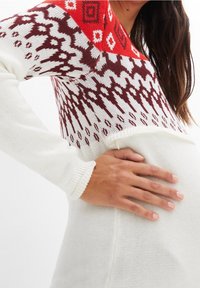 Pull en tricot blanc avec un design géométrique rouge et brun sur la partie supérieure, doté de manches longues et d'une coupe ample au niveau de la taille.