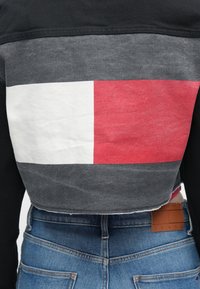 Lühendatud jakk, millel on must esikülg, hall tagakülg punaste ja valgete ristkülikukujuliste mustritega ning narmendav ääris. Kandmisega sinised teksapüksid.