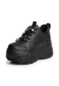 Zwarte platform sneaker met een dikke zool en decoratieve zilveren bedels bevestigd aan de veters op een witte achtergrond.