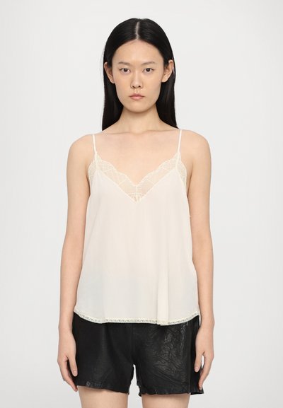 Débardeur beige clair avec un garniture en dentelle, décolleté en V, bretelles ajustables et une silhouette fluide, associé à des shorts noirs.