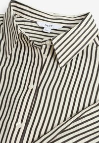 Chemise blanche boutonnée avec des rayures verticales noires et un col pointu, avec une étiquette de la marque "NEXT" à l'intérieur de l'encolure.