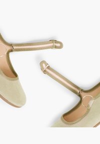 Hellgrüne Wildlederschuhe mit runder Zehenpartie verfügen über elastische Riemen und eine kreisförmige Hardware-Akzentuierung. Die Innensohle ist beige und hat eine weiche Textur.