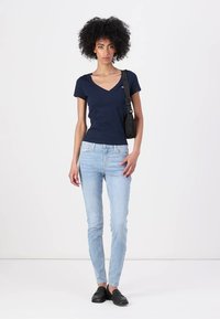 Marineblå V-hals t-skjorte, korte ermer; lyseblå smale jeans; svarte slip-on sko; skulderveske med stropp; glatt tekstur.