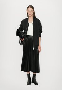 Giubbotto bomber nero, top bianco, gonna plissettata nera e stivaletti neri alla caviglia. Tessuto liscio, chiusura con zip e borsa elegante con finitura lucida.