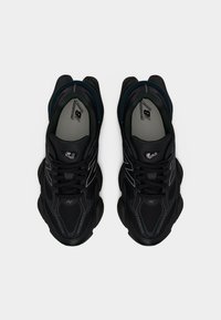 Ζευγάρι μαύρα παπούτσια τρεξίματος New Balance με χοντρές σόλες, πάνελ από δίχτυ και αντανακλαστικές λεπτομέρειες, σε ουδέτερο φόντο, φωτογραφία από πάνω.