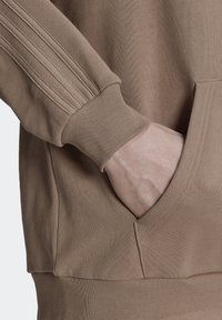 Brun sweatshirt med ribbade muddar och sidoseam. Har en framficka med en mjuk, texturerad yta.