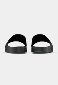 Fekete gumiból készült papucs nyitott sarokkal, texturált talppal és oldalán vízszintes barázdákkal a jobb tapadás és esztétikai részlet kedvéért.