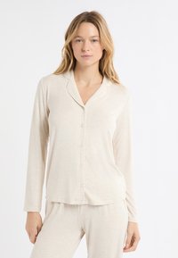 Beżowa piżama z kołnierzykiem, długimi rękawami i zapięciem na guziki; wykonana z miękkiego, lekkiego materiału o delikatnej fakturze.