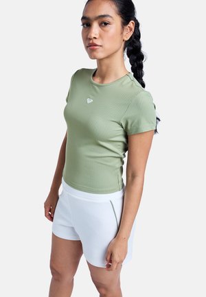 Top de manga corta con textura acanalada en verde apagado, combinado con pantalones cortos blancos con bolsillos. El top tiene un pequeño logo de color claro en el pecho.