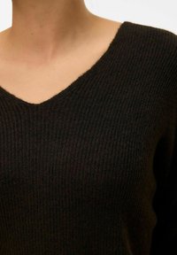 Černý pletený svetr s výstřihem do V. Materiál je hřebíčkový a látka vypadá měkce a teple.