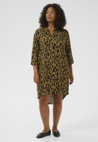 Leopard-print kjole i brune og sorte nuancer, med krave, trekvartærmer og en let længere bagkant. Flade sorte sko.