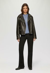 Czarna skórzana kurtka motocyklowa z srebrnymi detalami, nałożona na jasnoniebieską koronkową bluzkę, w zestawie z czarnymi spodniami dzwonami i czarnymi butami.