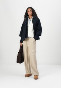 Navy oversized jacket, cream ribbed sweater, light blue shirt, beige wide-leg cargo pants, brown bag, and tan platform shoes.