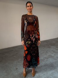 Διάφανο μαύρο φόρεμα με πολύπλοκα πολύχρωμα μοτίβα, μακριά μανίκια, εφαρμοστή σιλουέτα και φαρδιά φούστα, συνδυασμένο με μπεζ τακούνια με στρας.