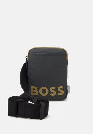 Czarna nylonowa torba na ramię z złotym logo "BOSS", prostokątny kształt, górne zapięcie na zamek błyskawiczny oraz regulowany czarny pasek.