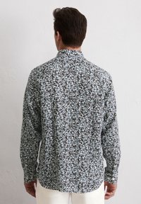 Langarmhemd mit einem gemusterten Design, das dunkle Blätter auf hellem Blau zeigt, aus leichtem Stoff gefertigt. Mit Knopfkragen.