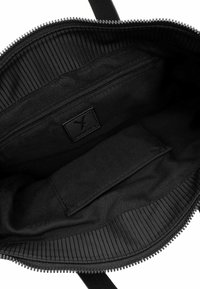 Svart tote-väska inuti med texturerat tyg, en ficka med dragkedja och ett platt fack. Har ribbat detaljer längs dragkedjeöppningen.