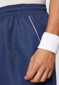 Navy athletic shorts with a textured finish, featuring a white piping detail and an elastic waistband. A white wristband is visible.