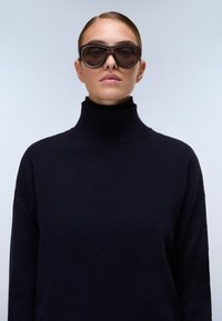 Schwarzer Rollkragenpullover mit einer weichen Textur und lässiger Passform, kombiniert mit übergroßen dunklen Sonnenbrillen mit runder Form und getönten Gläsern.