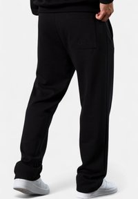 Schwarze Jogginghose mit lockerer Passform, mit einer Gesäßtasche und subtiler Logodetails. Hergestellt aus einem weichen Material, mit elastischen Bündchen an den Knöcheln.