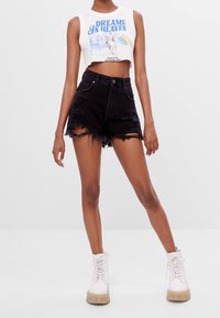 Débardeur blanc court avec un graphique "DREAMS IN HEAVEN" associé à un short en denim noir déchiré taille haute. Stylisé avec des bottes blanches à lacets.