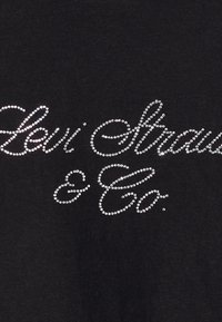 Svart bomull t-skjorte med "Levi Strauss & Co." trykt i glitrende sølv rhinestones, med et design i kursiv skrifttype.